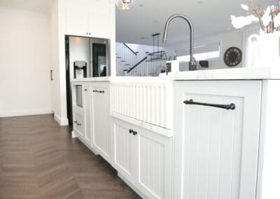 Close-up of a fireclay butler sink with matte black gooseneck tap on a marble-look island bench.