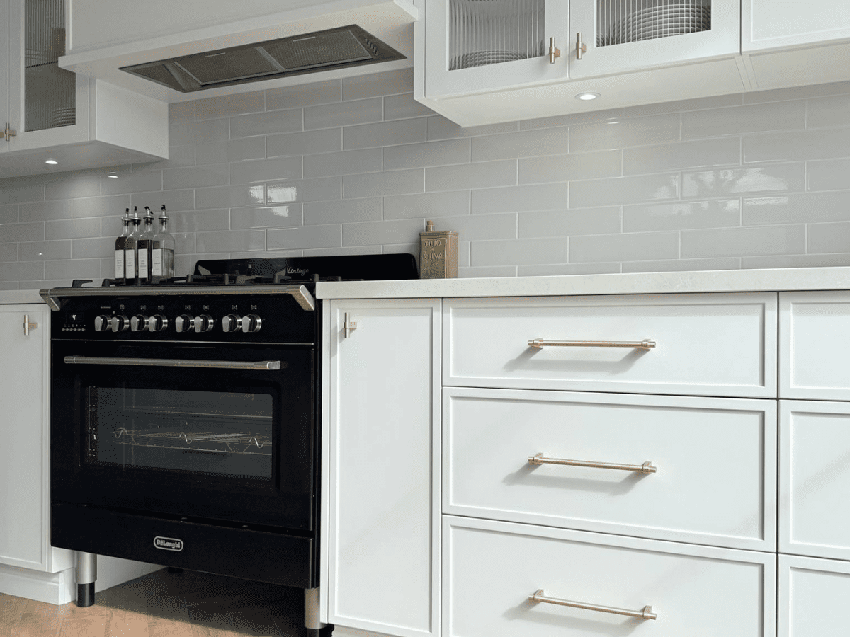 Modern white kitchen with gold handles on drawers and cabinets, featuring a black freestanding oven and glossy light grey subway tile backsplash.
