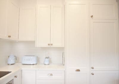Bright white kitchen with shaker-style cabinetry, marble-look benchtops, and pastel blue SMEG kettle and toaster.