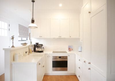 Compact white kitchen with shaker cabinetry, Calacatta-style benchtops, and soft blue SMEG appliances.