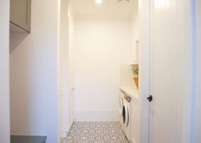 Elegant white laundry with shaker cabinets, front-load washer and dryer, patterned tiles, and a built-in sink.