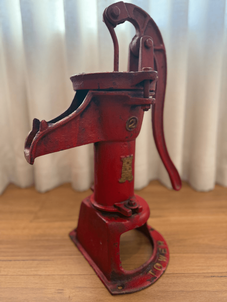 quality always pump A bright red water pump mounted on a wooden base, featuring a metal handle and a rustic, weathered finish.