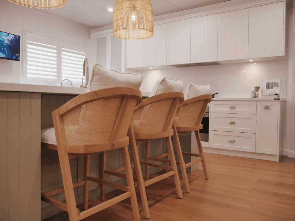 Bright white coastal kitchen display with timber bar stools and panelled cabinetry at the Harrington Kitchens showroom in South West Sydney.