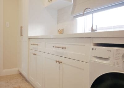 Hamptons-style laundry with white shaker cabinetry, stone benchtop, and front-load washer.