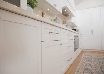 A white shaker-style kitchen featuring brushed nickel Zanda Mayfair handles and knobs, with Caesarstone Alpine Mist benchtops and splashback for a seamless, calming look.