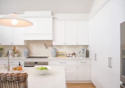 White shaker kitchen featuring brushed nickel Zanda Mayfair hardware with knobs on upper cabinets and pull handles below, paired with Caesarstone Alpine Mist benchtops and splashback for a seamless, calming design.