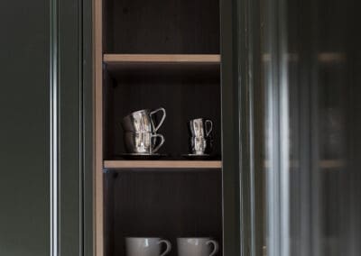 Open shelving in butler’s pantry featuring stacked silver espresso cups and white mugs against walnut timber interior.