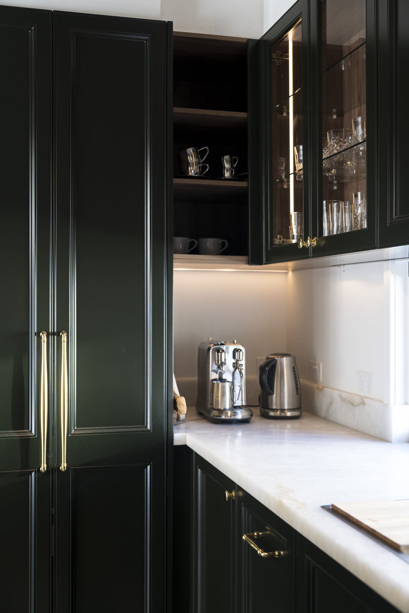 Butler’s pantry with deep green cabinetry, gold hardware, white stone benchtops, and a coffee station with espresso machine and kettle.