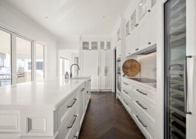 Elegant white shaker kitchen with quartzite island, herringbone flooring, induction cooktop, and integrated wine fridge.