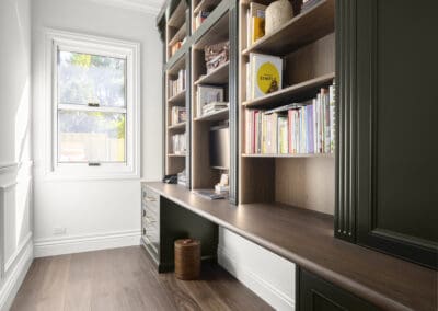 Elegant home study with dark green cabinetry, timber benchtop, and full-height bookshelves.