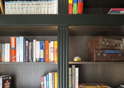 Close-up of custom study shelving in deep green with timber backing, featuring books and decorative items.