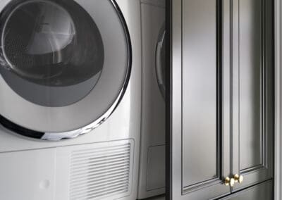 Laundry with dark shaker cabinetry, gold hardware, and stacked Miele washer and dryer.