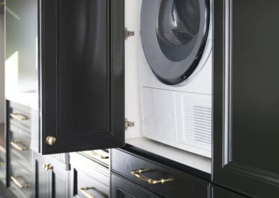Laundry area with concealed Miele washer and dryer behind deep green shaker cabinetry with gold hardware.