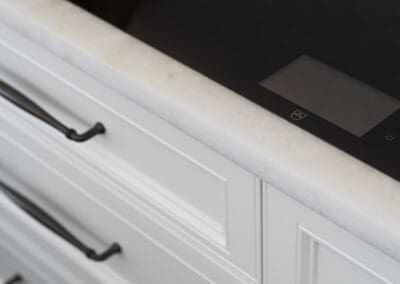 Close-up of a white quartzite benchtop with a sleek black induction cooktop and classic white provincial drawers.