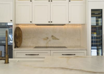 Close-up of a quartzite splashback and induction cooktop framed by white cabinetry with under-cabinet lighting.