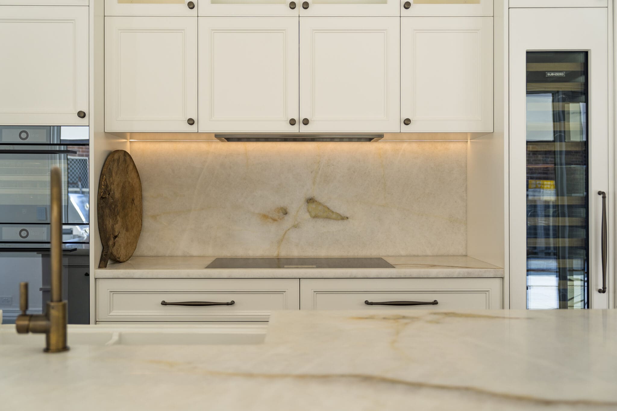 Close-up of a quartzite splashback and induction cooktop framed by white cabinetry with under-cabinet lighting.