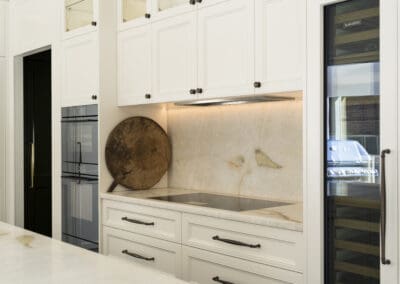 White provincial kitchen featuring a quartzite splashback, induction cooktop, double ovens, and integrated wine fridge.