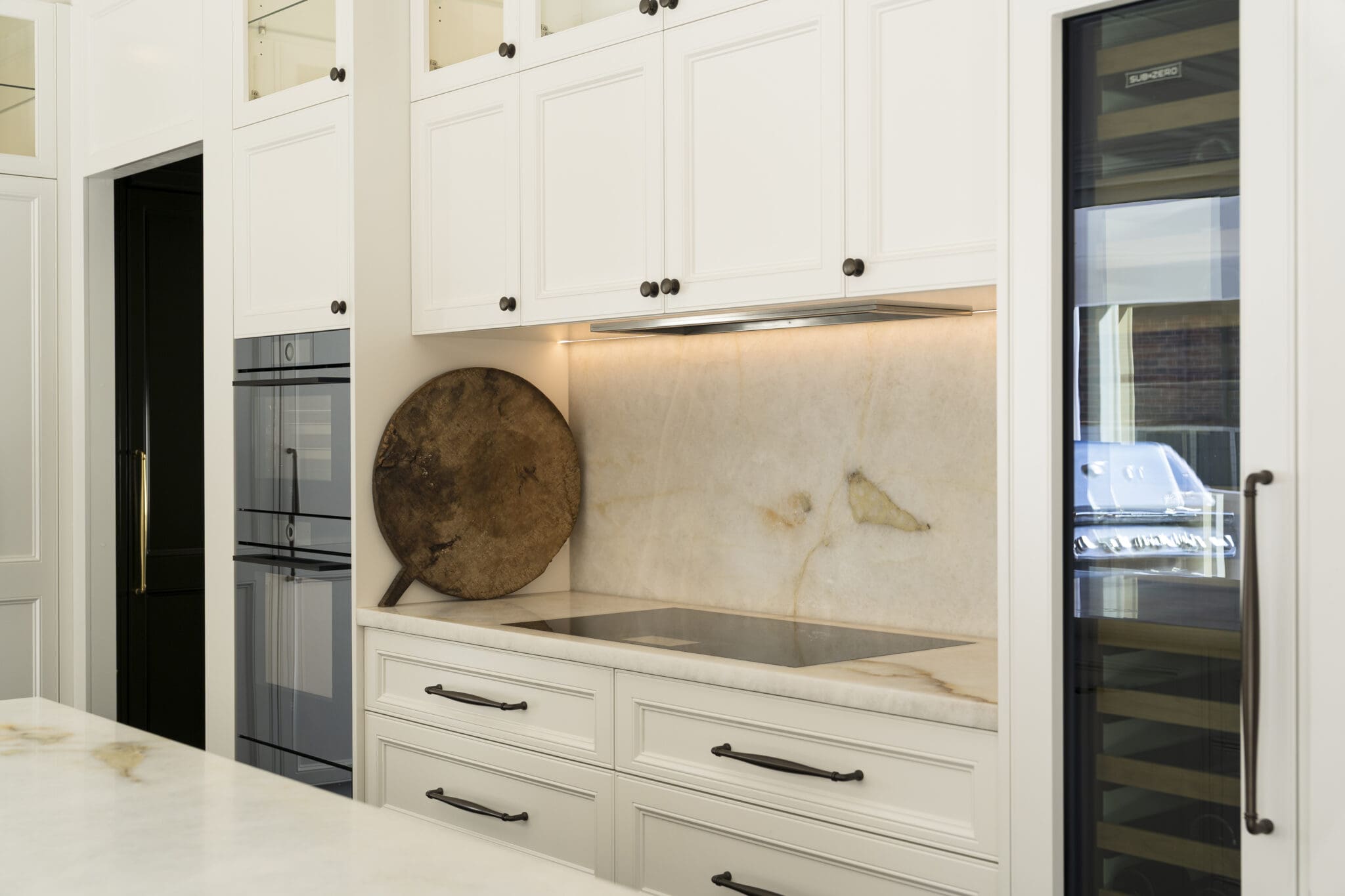 White provincial kitchen featuring a quartzite splashback, induction cooktop, double ovens, and integrated wine fridge.