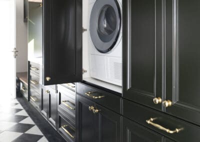 Laundry area with concealed Miele washer and dryer behind deep green shaker cabinetry with gold hardware.