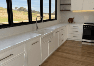 Light-filled white country kitchen featuring white colorado cabinetry, black-framed windows, and farmhouse sink.