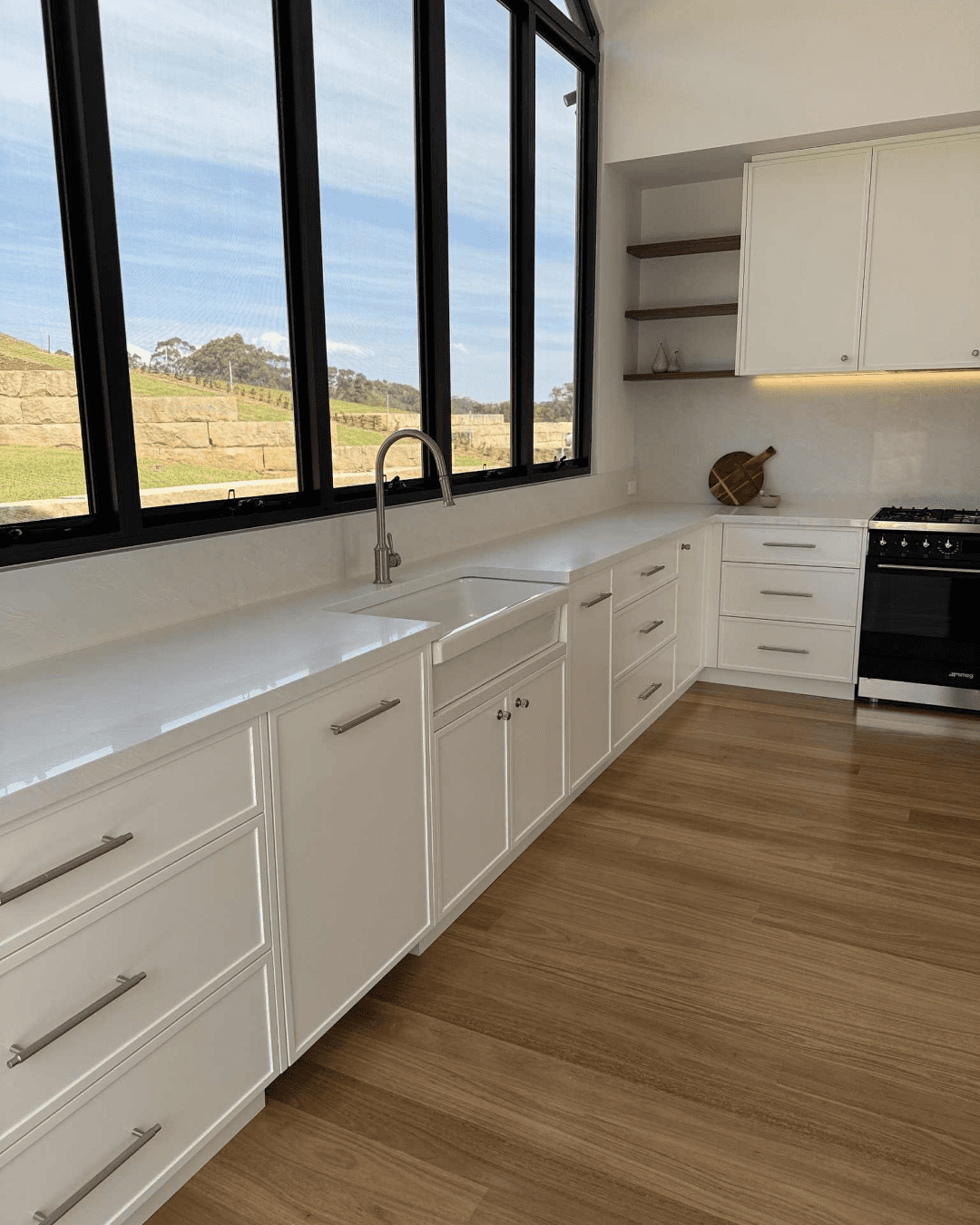 Light-filled white country kitchen featuring white colorado cabinetry, black-framed windows, and farmhouse sink.