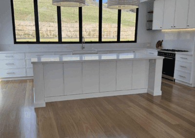 Modern country kitchen in Picton with vaulted ceilings, black-framed windows, white island benchtop, pendant lights, timber floors, and custom white cabinetry.