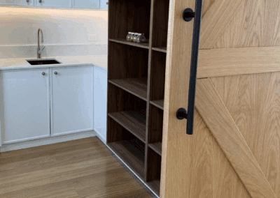 Modern butler’s pantry with white cabinetry, wooden shelving, timber barn door with black handle, and soft under-cabinet lighting in a Picton home kitchen.