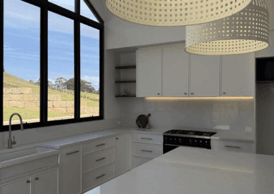 sundrenched white country kitchen featuring shaker cabinetry, black-framed windows, and timber floors with a countryside outlook.
