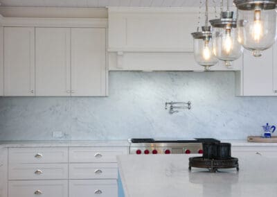 White shaker kitchen with marble backsplash, Wolf freestanding oven, integrated Qasair rangehood cabinetry, Sub-Zero wine cooler, and marble island.
