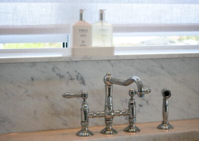 Polished chrome kitchen taps with Carrara marble splashback extending up to the windowsill.