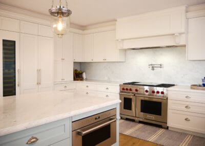 White shaker kitchen with marble backsplash, Wolf freestanding oven, integrated Qasair rangehood cabinetry, Sub-Zero wine cooler, and marble island.