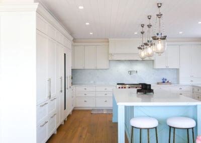 Custom white shaker cabinets with blue two-tone island, Carrara marble benchtops and pendant lights overhead.