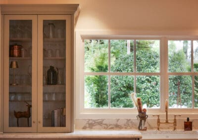 Country-style kitchen with custom joinery appliance cupboard next to window, featuring hidden storage, classic cabinetry, and natural light.