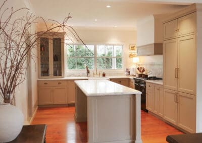 Kitchen with central island, brass accents, farmhouse sink, and large windows bringing natural light onto timber flooring.