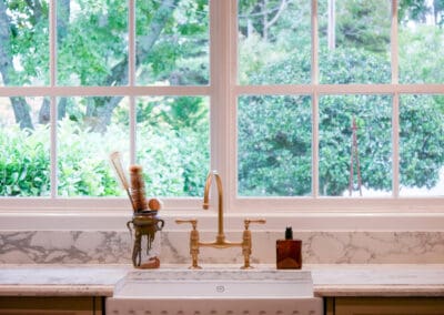Farmhouse kitchen sink with brass tapware, marble splashback, and large window with natural light