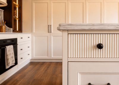 Close-up of fluted kitchen drawer fronts with brass knob, stone benchtop edge and custom cabinetry.