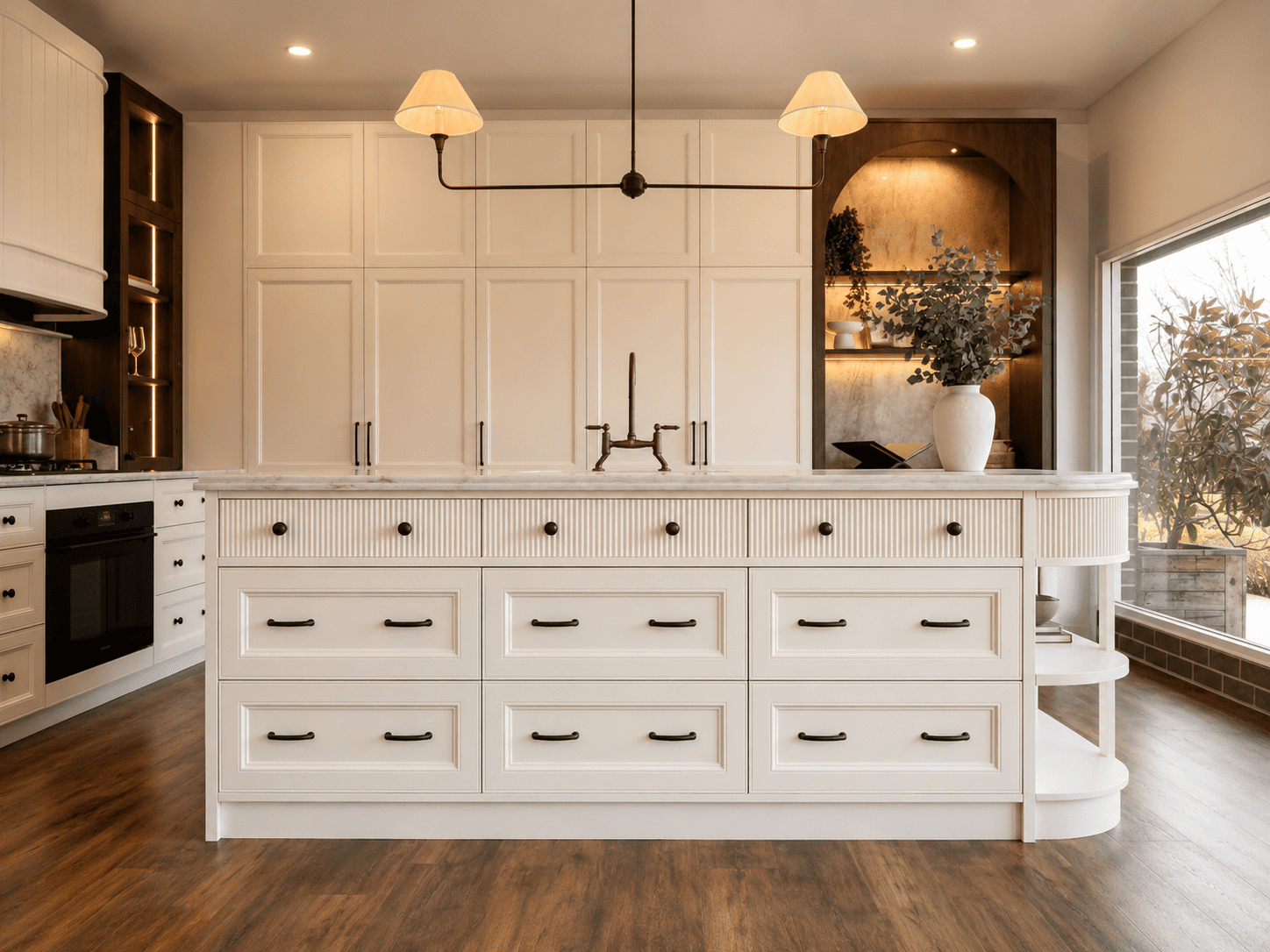 Front view of a fluted kitchen island with stone benchtop, provincial drawers and floor-to-ceiling cabinetry in the background.