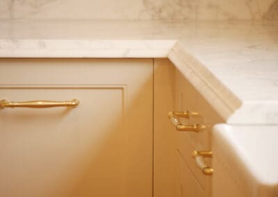 Close up of soft beige Waratah-profile cabinetry with polished gold bar pull handles against marble benchtop edge in heritage Sydney kitchen