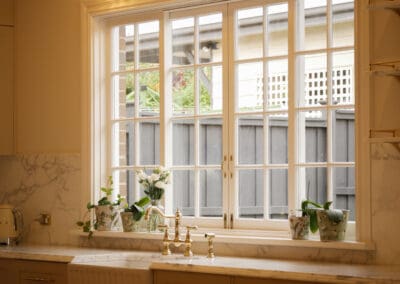Close up of polished gold bridge mixer tap and Turner Hastings sink set into marble benchtop beside window with white flowers in heritage Sydney kitchen