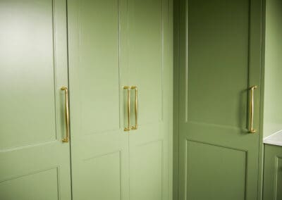 Close up of full-height green Waratah-profile laundry storage cabinetry with polished gold pull handles in heritage Croydon Park laundry renovation