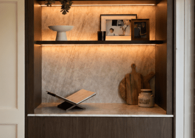 Custom display nook with timber cabinetry, stone feature wall and illuminated shelves.