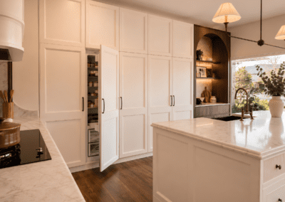 Tall pantry cabinets with integrated storage beside a cream kitchen island with stone benchtop and bronze tapware.
