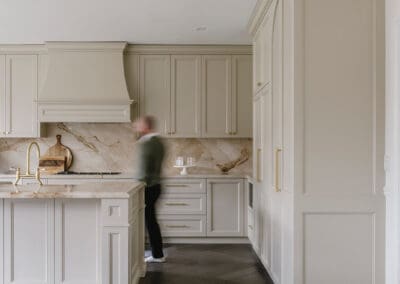 Classic luxury kitchen with handcrafted cabinetry, stone benchtops and a blurred figure walking through the space, showcasing everyday family living.