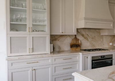 Custom classic kitchen featuring an arched glass display cabinet with chiefly cabinetry, satin brass handles and elegant traditional detailing.